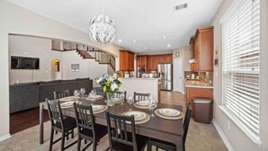 Une cuisine moderne avec des meubles en bois, un îlot central et un coin repas agrémenté d’un lustre.
