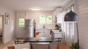 A modern kitchen with white cabinets, a stainless steel refrigerator, and a dining area with a table and chairs. - 117 Wainaku St, Hilo, Unit C (Hilo)