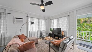 A modern living room with a sofa, armchair, and coffee table, a TV, and a ceiling fan. - 117 Wainaku St, Hilo, Unit C (Hilo)