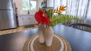A kitchen with white cabinets, a stainless steel refrigerator, and a dining table with a woven placemat. - 117 Wainaku St, Hilo, Unit C (Hilo)