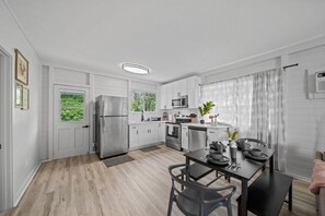 Et moderne køkken med hvide skabe, rustfrie stålapparater og et spiseområde med et bord og stole.