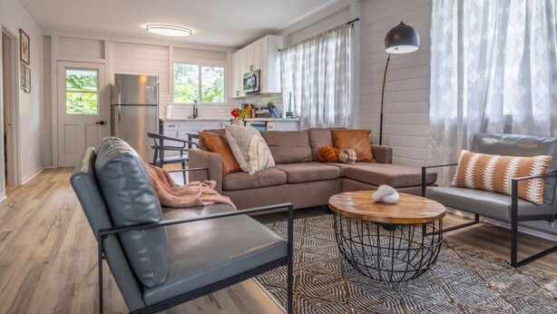 A modern living room with a sofa, coffee table, and a dining area with chairs. - 117 Wainaku St, Hilo, Unit C (Hilo)