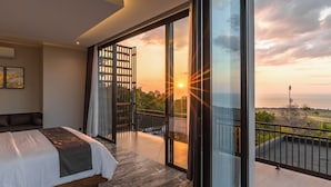 A modern bedroom with a large bed, a balcony with a view of the sunset, and a glass door leading to an outdoor area. - Villa Lovina Hill Paradise (Banjar)