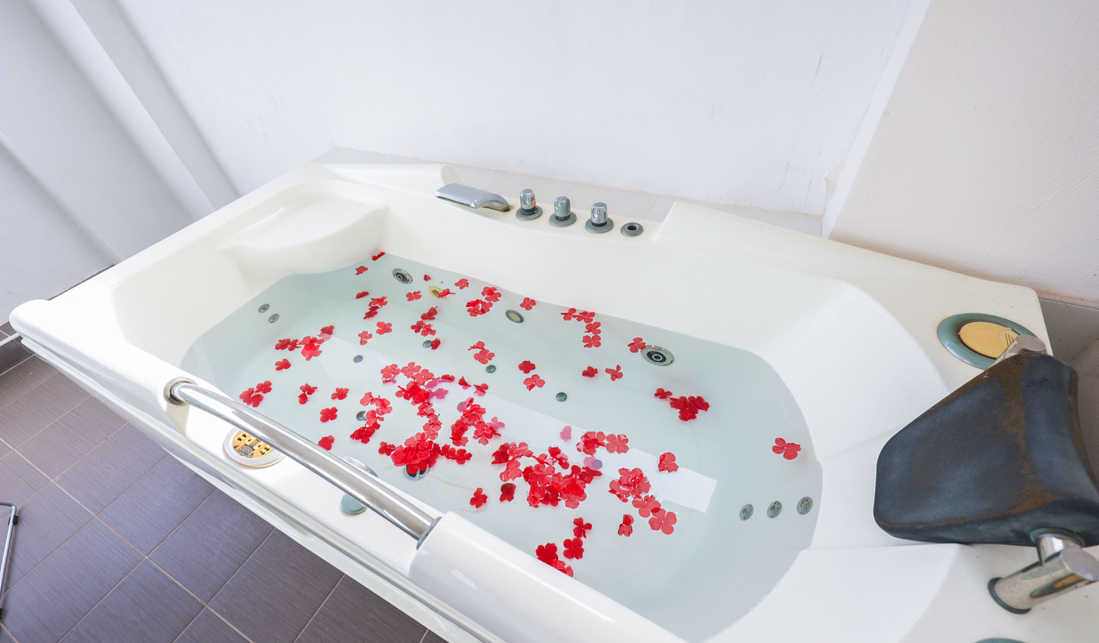 A bathtub with red flower petals floating in the water, a faucet, and a showerhead.