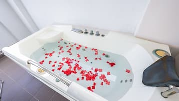 A bathtub with red flower petals floating in the water, a faucet, and a showerhead.