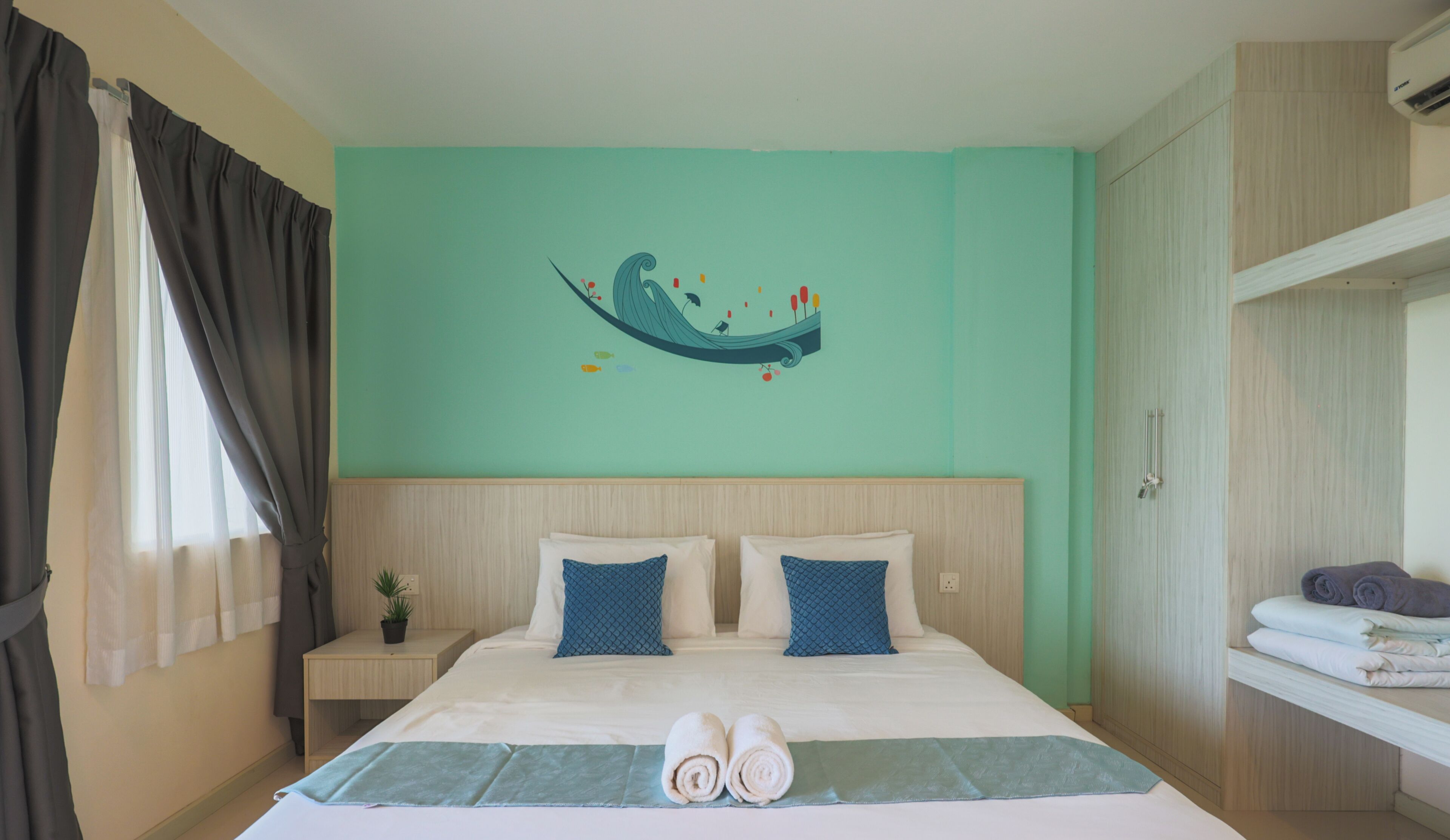 A hotel room with a bed, a nightstand, a wall-mounted air conditioner, and a window with curtains.
