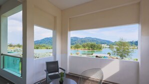 A balcony with a view of a lake and mountains, a chair, and a table with a plant.