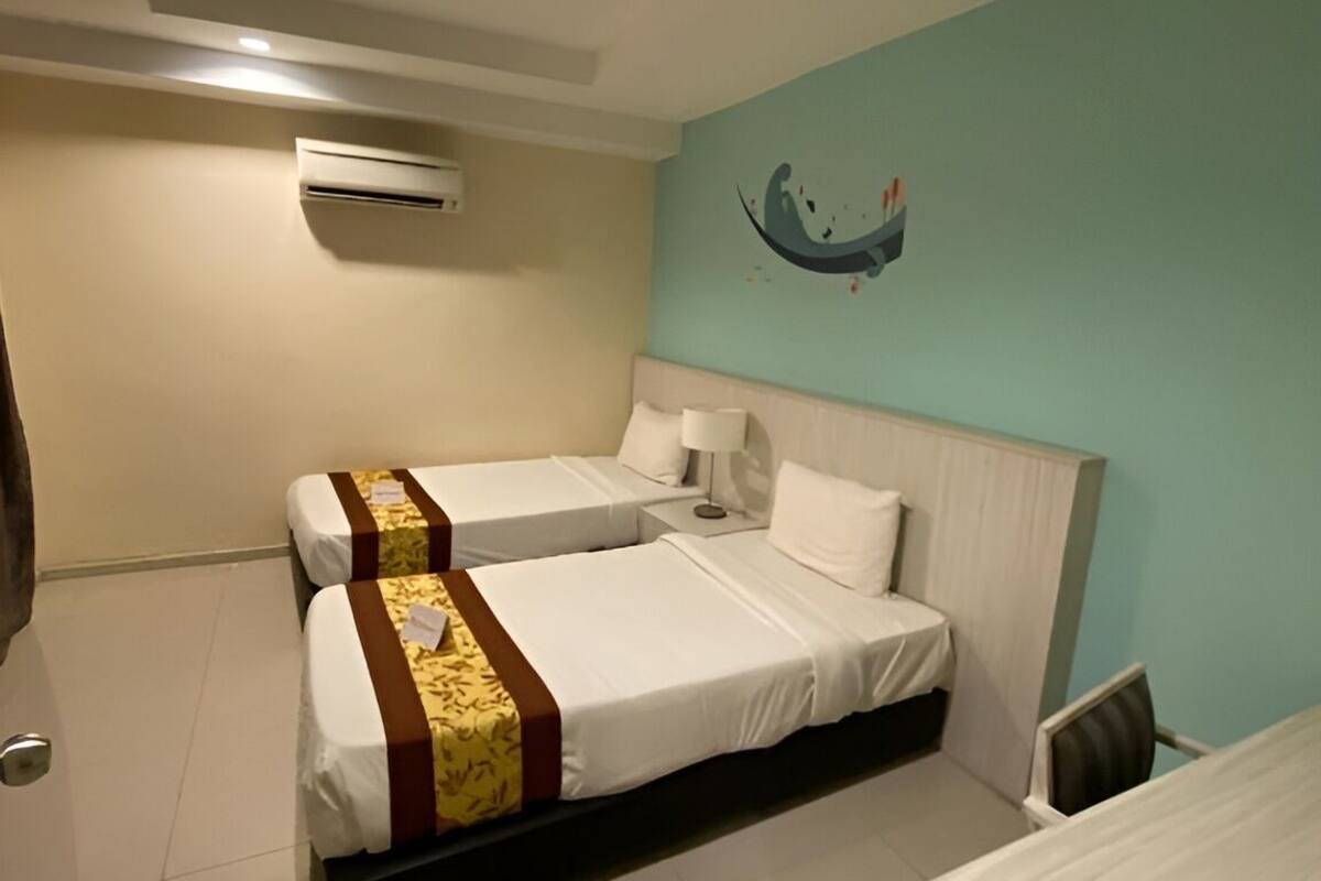 Een hotelkamer met twee bedden, een bureau en een luchtverkoeler aan de muur.