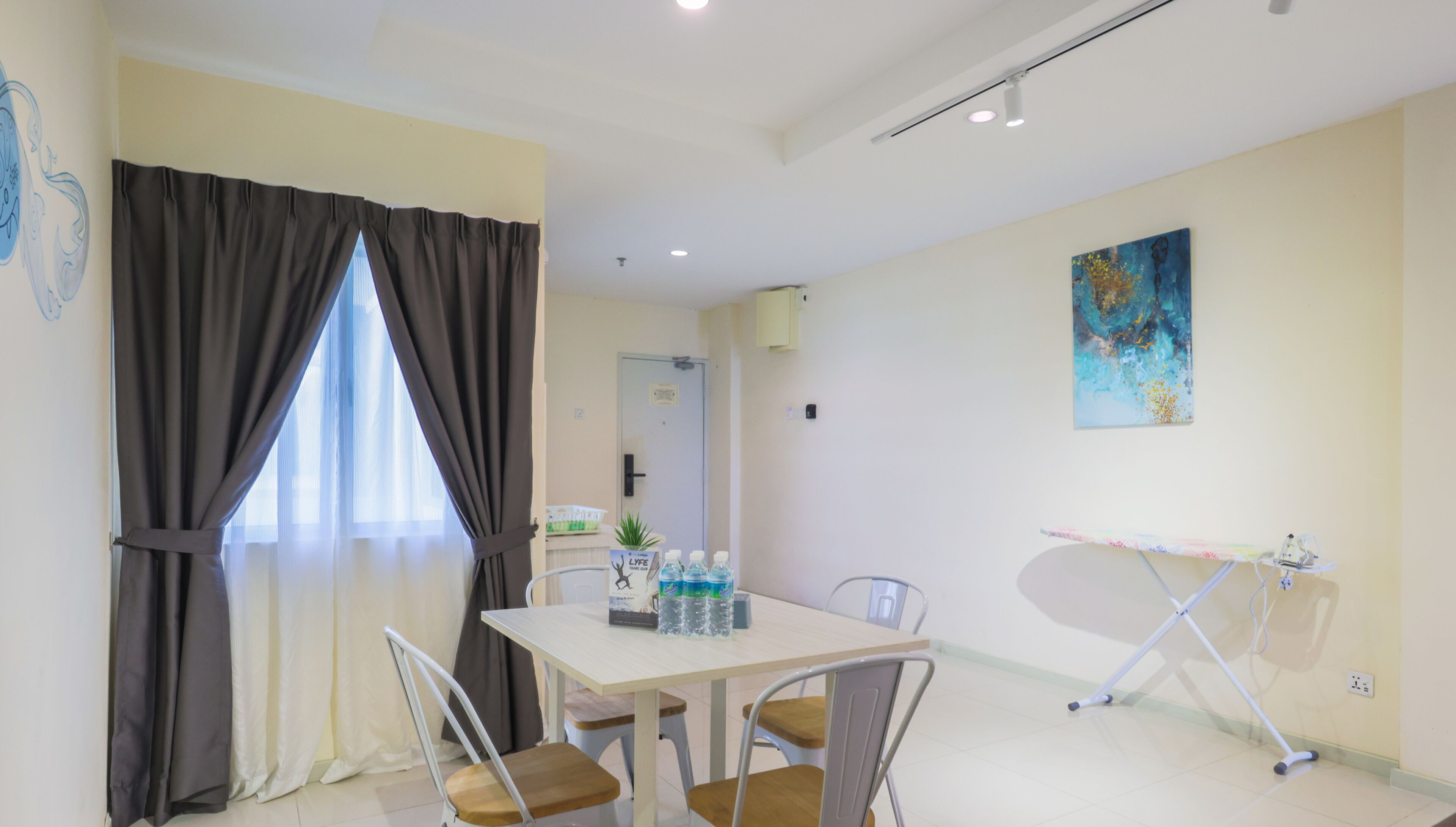 A room with a dining table, chairs, a water dispenser, a painting on the wall, and a door in the background.