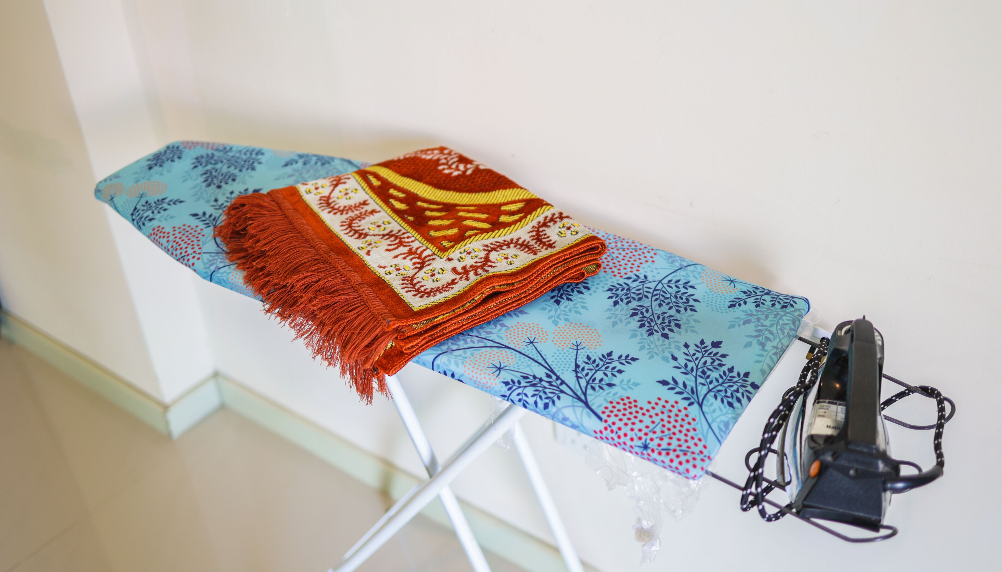 Una tabla de planchar con un paño azul estampado, un paño doblado rojo y beige, y un planchador.