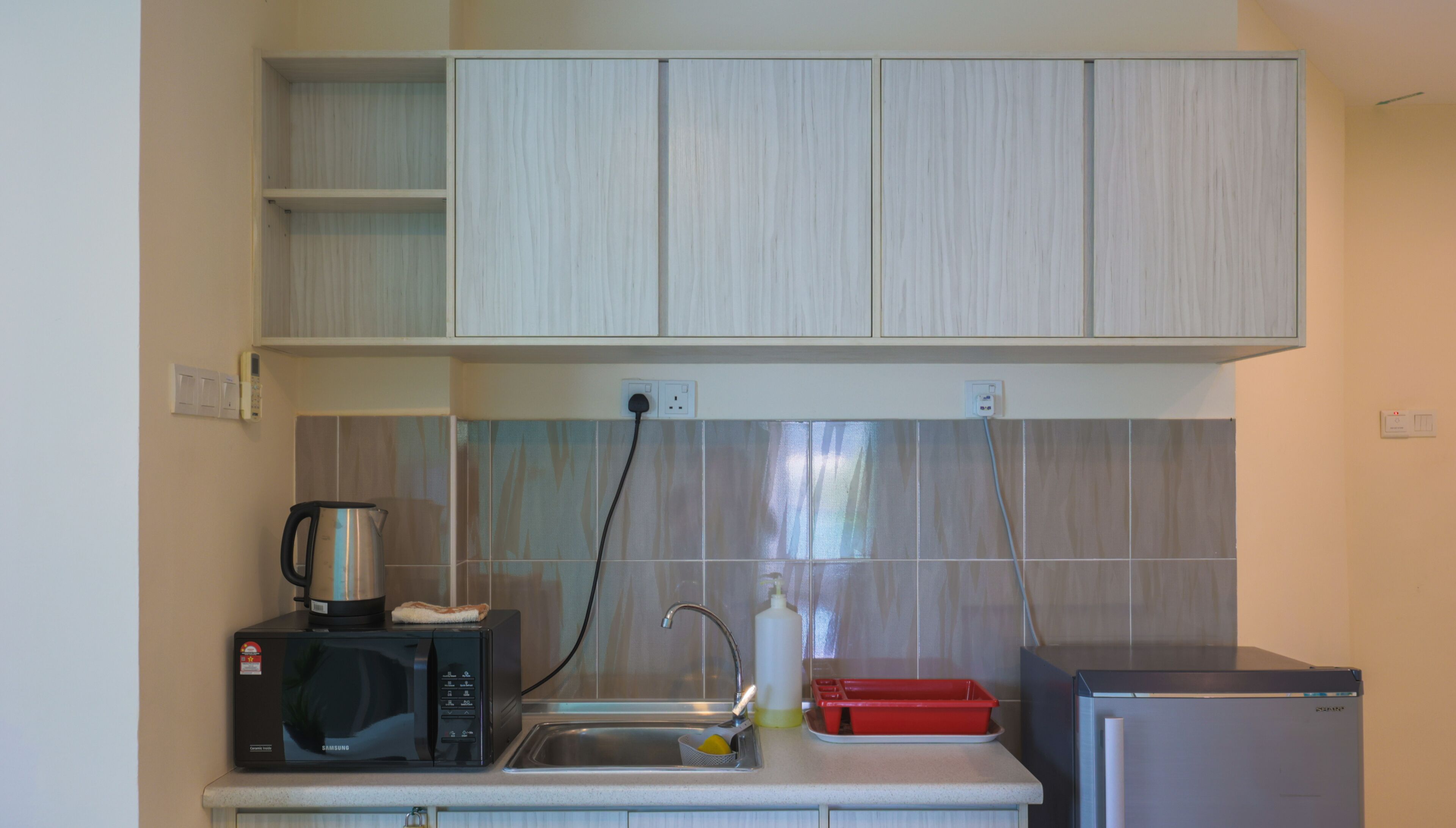A compact kitchen with a microwave, kettle, sink, and a small refrigerator.