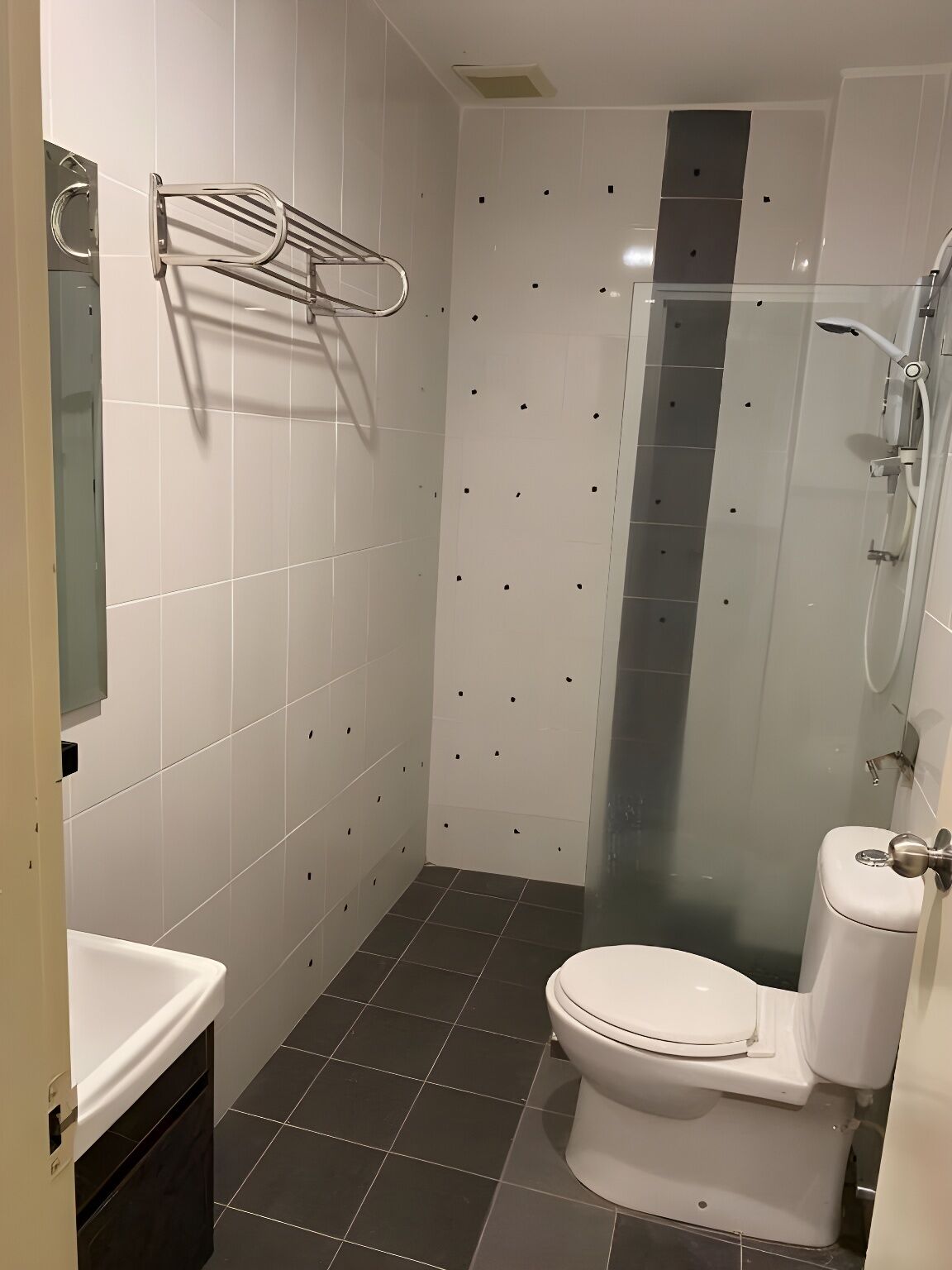 Une salle de bain moderne avec des carreaux blancs, une douche en verre, des toilettes blanches et un porte-serviettes.