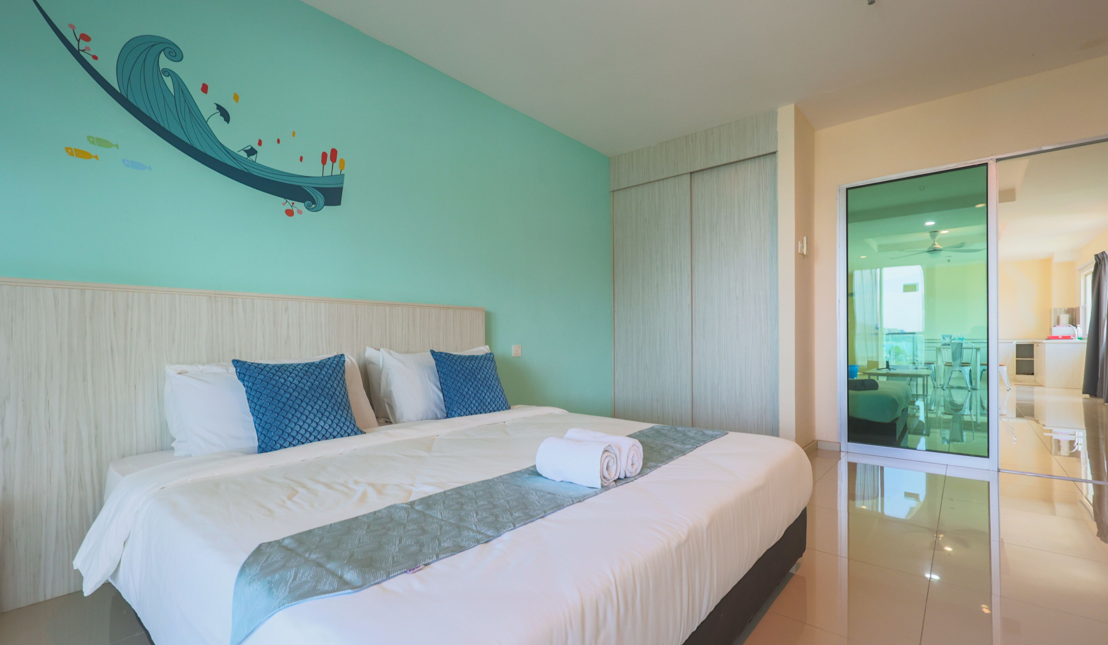 A modern hotel room with a large bed, a decorative wall mural, and a glass door leading to a dining area.