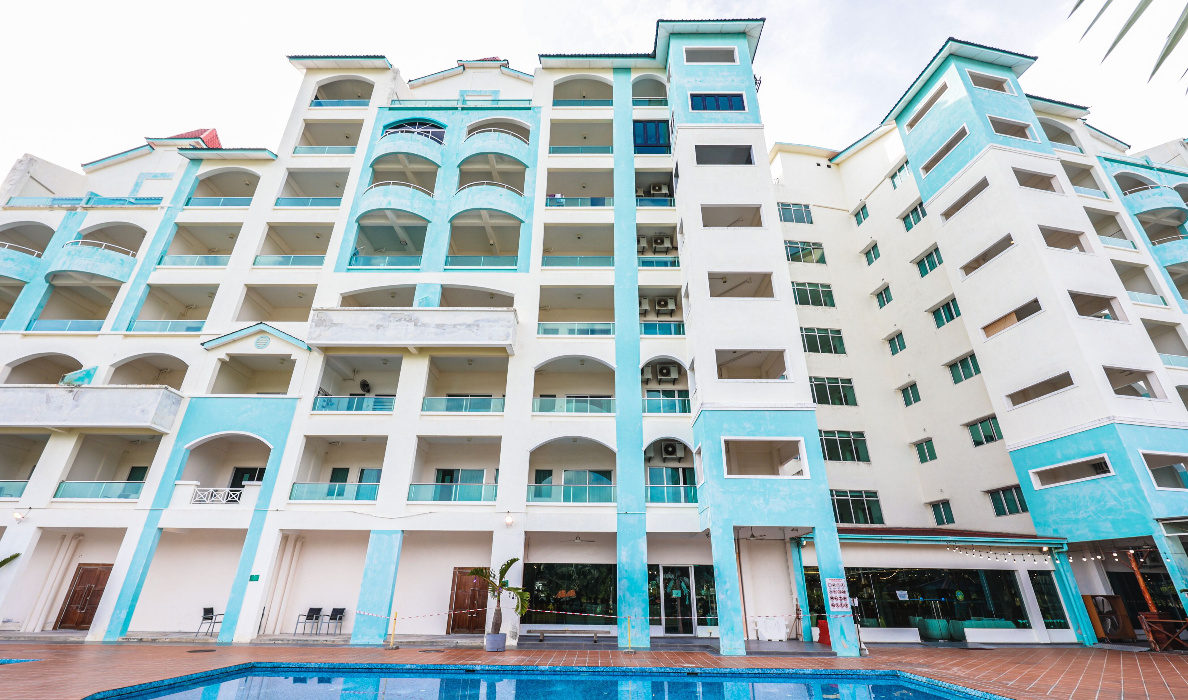 Ein mehrstöckiges Hotel mit Poolbereich, ausgestattet mit Balkonen und einem modernen architektonischen Design.