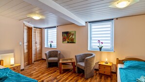 A room with a wooden floor, a bed with a blue bedspread, two upholstered chairs, a small wooden table, a nightstand with a lamp, and a window with blinds. - Apartment 'Ferienwohnung 2' with Wi-Fi (Ubstadt-Weiher)