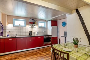 Una cocina con armarios rojos, piso de madera, una mesa de comedor con mantel a cuadros y un reloj en la pared.