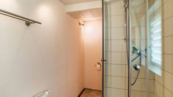Eine begehbare Dusche mit Glastrennwand, einer Handbrause, einem Handtuchhalter und einem Toilettenpapierhalter an der Wand.
