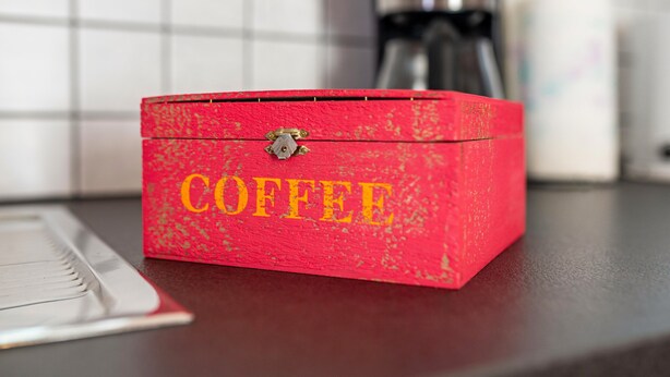 Een rode doos met de tekst 'COFFEE', geplaatst op een aanrecht.