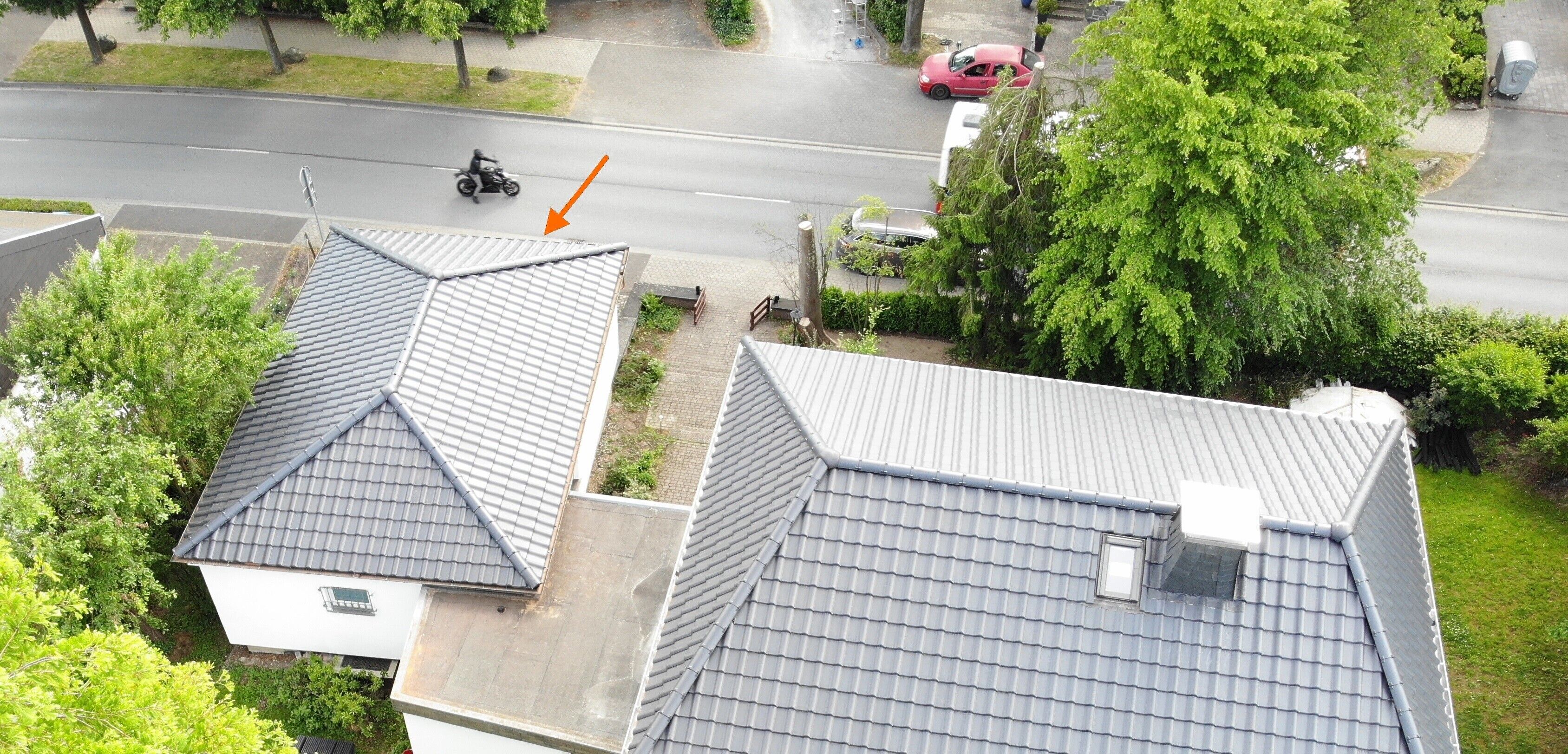 Área residencial com duas casas, uma com telhado triangular e outra com telhado plano, cercada por árvores e uma rua com carros estacionados.