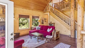 Una sala de estar acogedora con un sofá rojo, suelo de madera, una escalera y un ventanal grande.