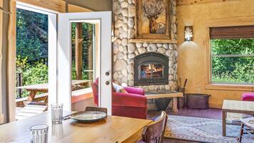 A cozy interior with a stone fireplace, wooden furniture, and large windows offering a view of the outdoors.