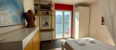 A bedroom with a bed, a map on the wall, a wardrobe, and a balcony with a view of the sea.