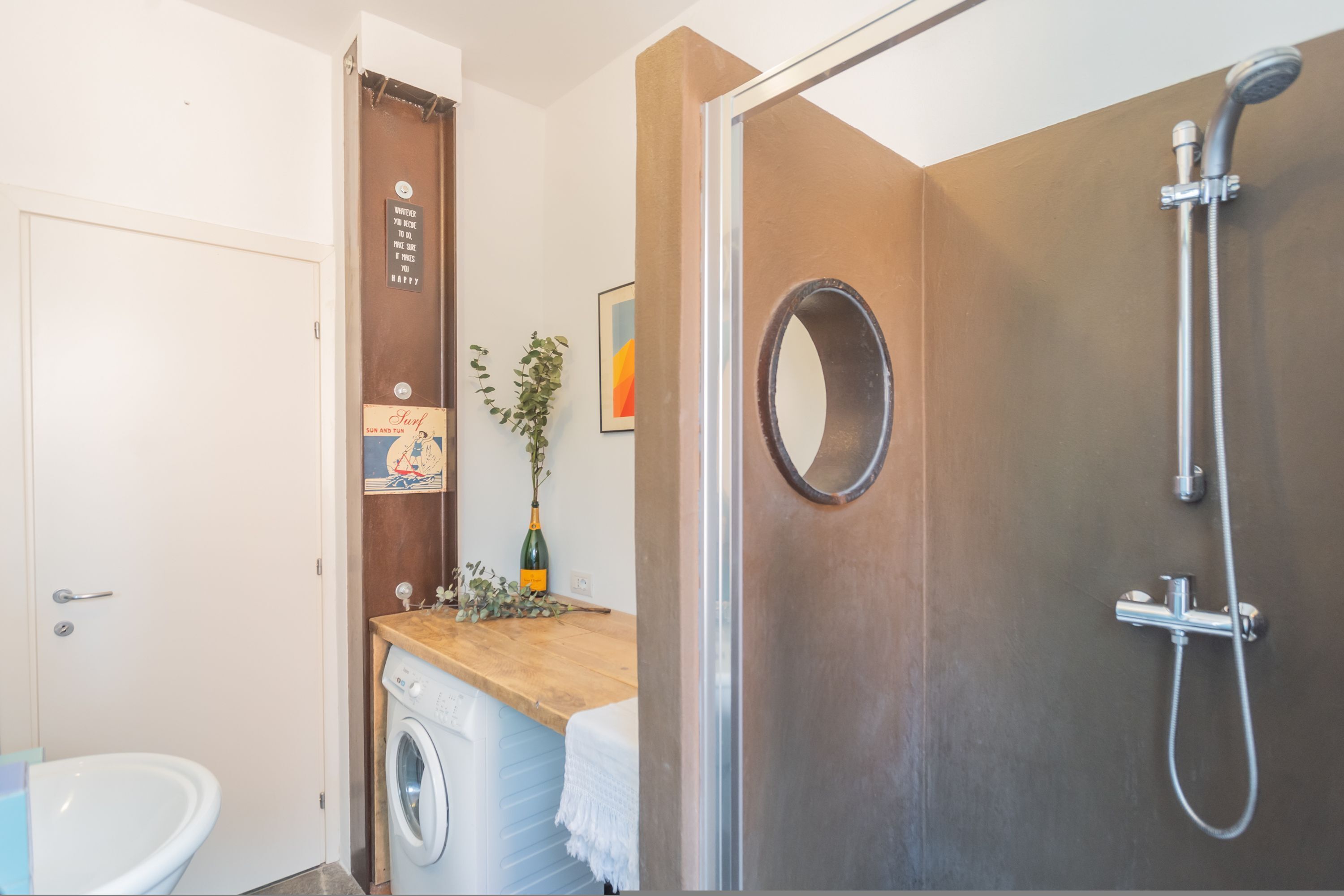 A bathroom with a shower, a washing machine, a sink, and a toilet.