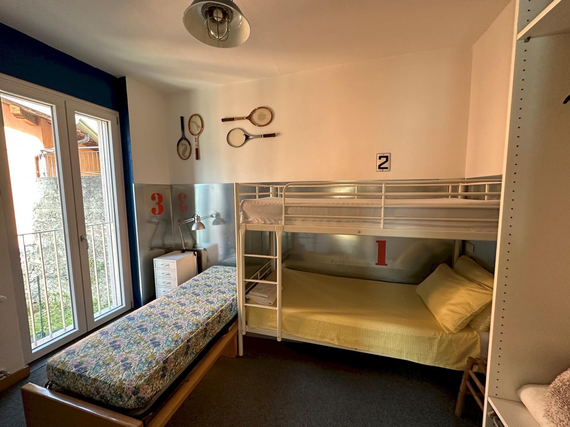 Une chambre avec un lit superposé, une fenêtre, un bureau et une lampe.