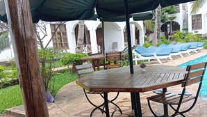 A wooden table with a green canopy, a stone patio, and a pool area with lounge chairs. - Charming two bedroom villa with WiFi, AC in fantastic Diani (Diani)