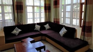 A living room with a sectional sofa, a wooden coffee table, and large windows with curtains. - Charming two bedroom villa with WiFi, AC in fantastic Diani (Diani)
