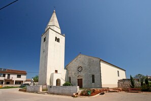 Una iglesia con un campanario y el edificio principal, rodeada por una zona pavimentada con bancos.