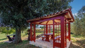 A gazebo with a stone base and red wooden structure, surrounded by trees and a picnic table. - Pool Villa Divina (Liznjan)