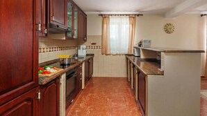 A kitchen with wooden cabinets, a tiled backsplash, a window with curtains, and a clock on the wall. - Pool Villa Divina (Liznjan)