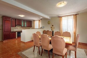 Un comedor con una mesa redonda y ocho sillas, una cocina con armarios de madera y un reloj en la pared.