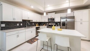 Cocina moderna con armarios blancos, una isla central, electrodomésticos de acero inoxidable y un salpicadero de azulejos negros.