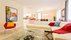 A modern living room with a glass coffee table, a red chair, a white sofa, and a kitchen in the background. - Spacious 5BR, Private Pool, Beautiful Decor (Davenport)
