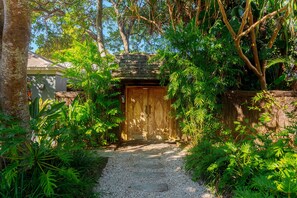 Stroll through lush gardens to a traditional door with intricate carvings, surrounded by tropical plants and a natural stone pathway.