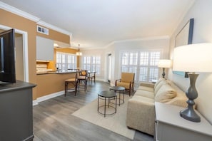 A modern living room with a sofa, coffee table, and chairs. There is a kitchen area with a refrigerator and a dining table. - Wyndham Kingstown Reef | 4BR King Suite w Balcony (Orlando)