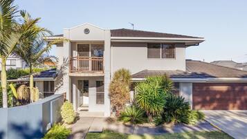 A two-story house with a balcony, a garage, and a well-maintained garden with palm trees.