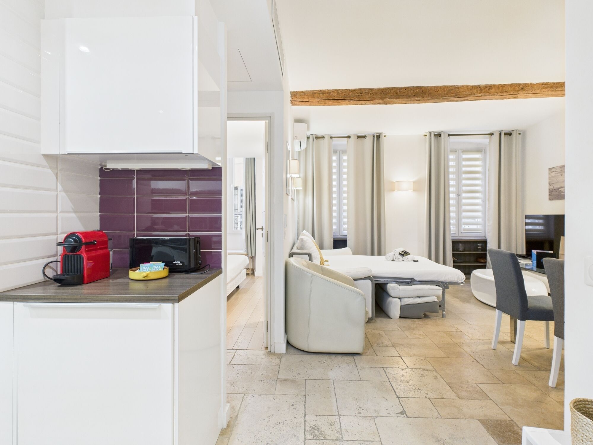Une chambre d’hôtel compacte comprenant un coin cuisine, un lit avec une petite table de chevet, un canapé, un coin repas avec une table et des chaises, et un téléviseur.