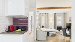 A compact hotel room with a kitchenette, a bed with a small bedside table, a sofa, a dining area with a table and chairs, and a TV. - Le Meynadier dans le centre historique (Cannes)