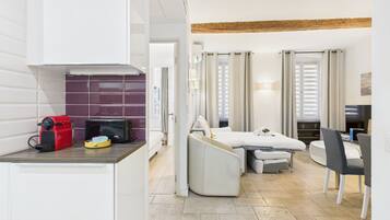 Une chambre d’hôtel compacte comprenant un coin cuisine, un lit avec une petite table de chevet, un canapé, un coin repas avec une table et des chaises, et un téléviseur.