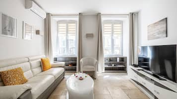 Un salon moderne avec un canapé, un pouf, une télévision et une vue dégagée grâce à de grandes fenêtres.