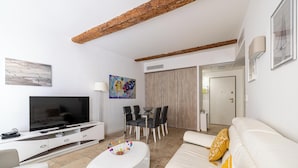 A modern living room with a flat-screen TV, a dining area with a table and chairs, and a sofa with a decorative pillow. - Le Meynadier dans le centre historique (Cannes)