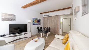 Un salon moderne doté d’un téléviseur à écran plat, d’un coin repas avec une table et des chaises, et d’un canapé agrémenté d’un coussin décoratif.