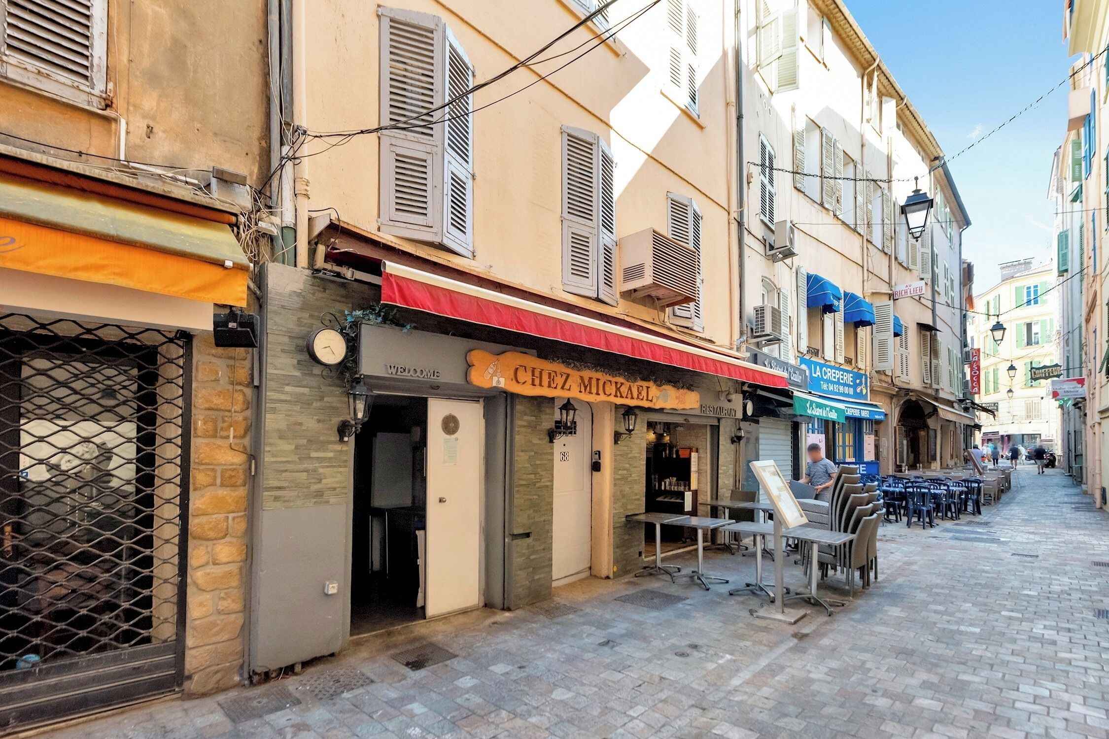 Une rue étroite où se trouvent un restaurant appelé « Chez Mikhail » et un café appelé « La Crêperie ».