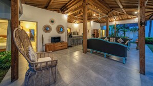 Un espacio habitable amplio con techo alto y vigas de madera, un sofá cómodo, una silla de mimbre y un televisor sobre un mueble de madera.