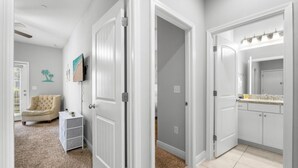 A hallway with a beige armchair, a small white side table, and a TV mounted on the wall. - Sandy Feet Retreat|Heart of Destin|Community Pool (Destin)