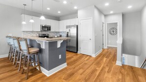A modern kitchen with a central island, bar stools, stainless steel appliances, and pendant lighting. - Sandy Feet Retreat|Heart of Destin|Community Pool (Destin)