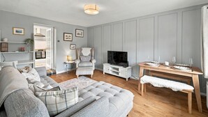 A living room with a sofa, armchair, TV, and a dining table set for two. - Heatherwood Cottage - Central Scone (Scone)
